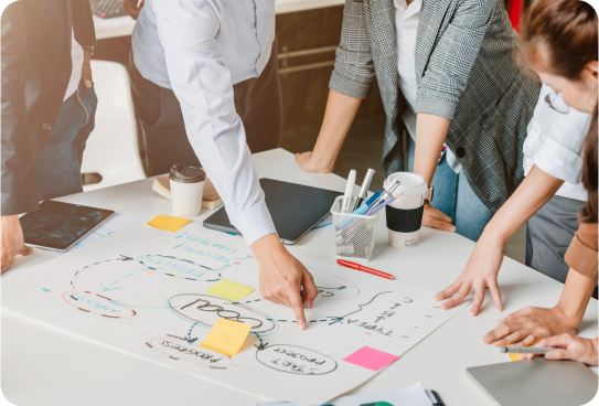 A group of consulting professionals standing around a table analyzing a strategy on paper.